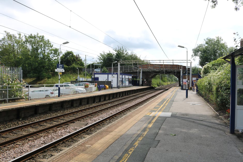 A view of Purley Oaks station platform showing double railway tracks with weathered wooden sleepers, bordered by a yellow line and tactile paving at the edge for safety. To the right, there is a narro